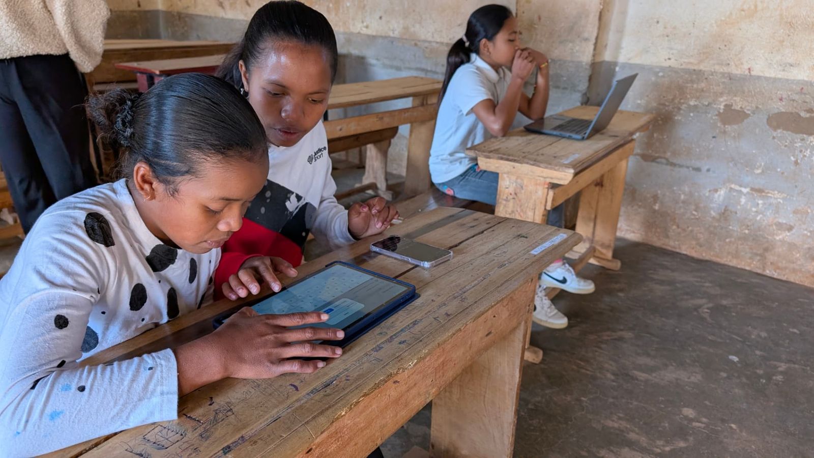 A student using a tablet while a classmate looks on, 2025