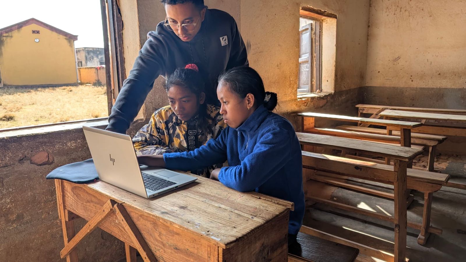 A trainer helping two students on a laptop in the classroom, 2025