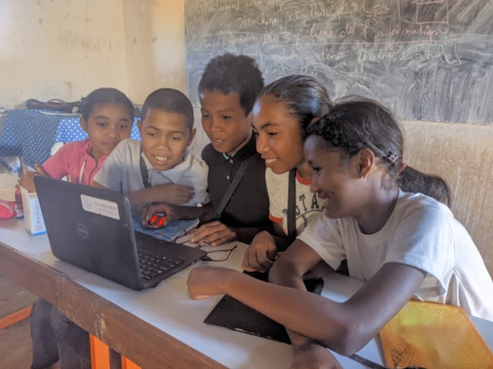 Five students crowded around a laptop in front of a blackboard, 2026